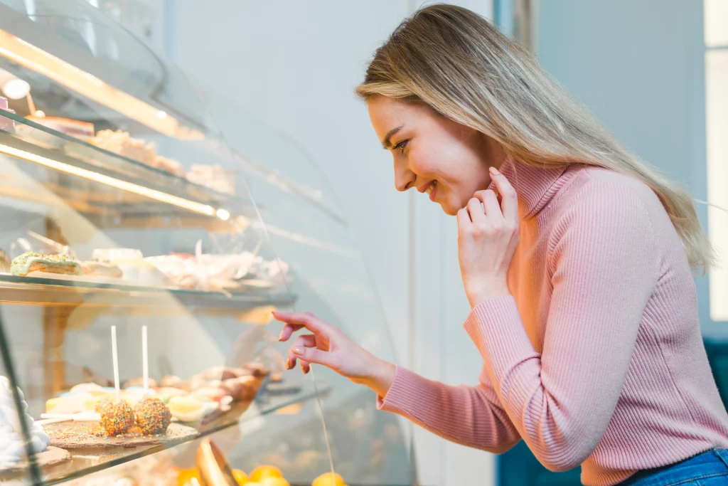 blonde-young-woman-looking-through-cake-display-cabinet-cafe